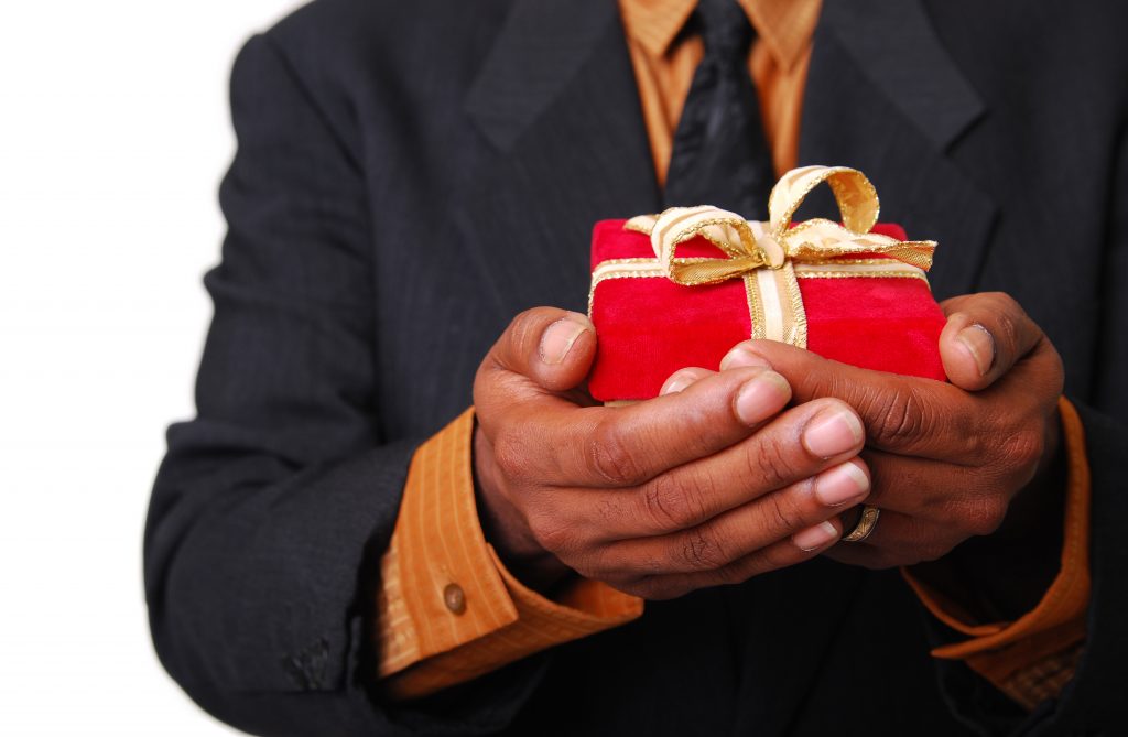 African-American male hands holding a red velvet box with gold ribbon.